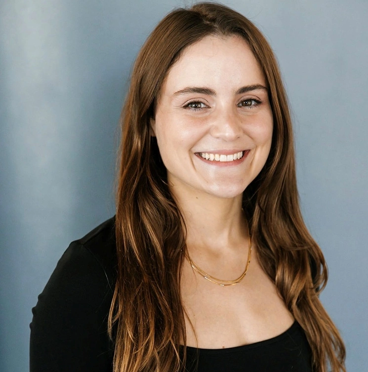 Professional headshot of smiling woman with long brown hair against blue background for dental practice.