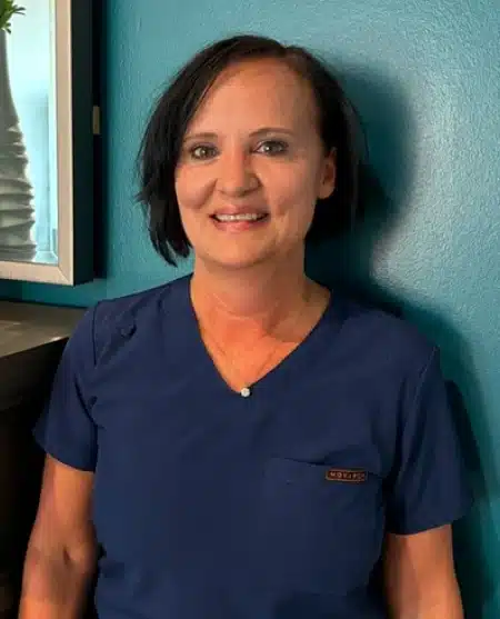 Woman with long dark hair smiling at camera against blue background, professional headshot.