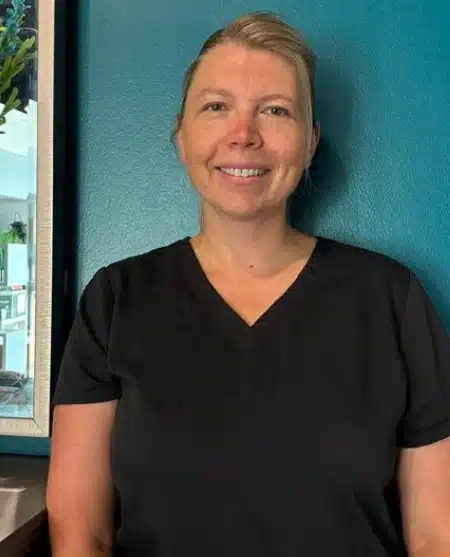 Woman smiling at camera wearing dental-themed shirt against blue background.