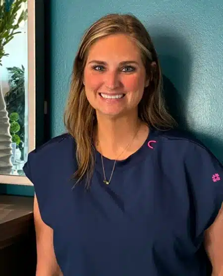 Woman smiling at camera wearing dental-themed shirt against blue background.