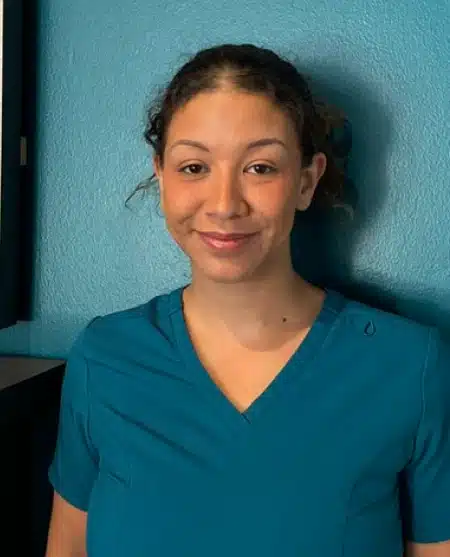 Woman with long dark hair smiling at camera against blue background, professional headshot.