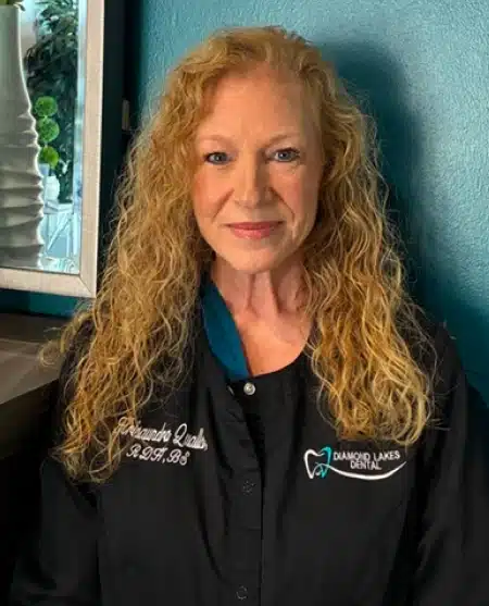 Professional headshot of woman with curly blonde hair wearing black polo shirt against blue background.