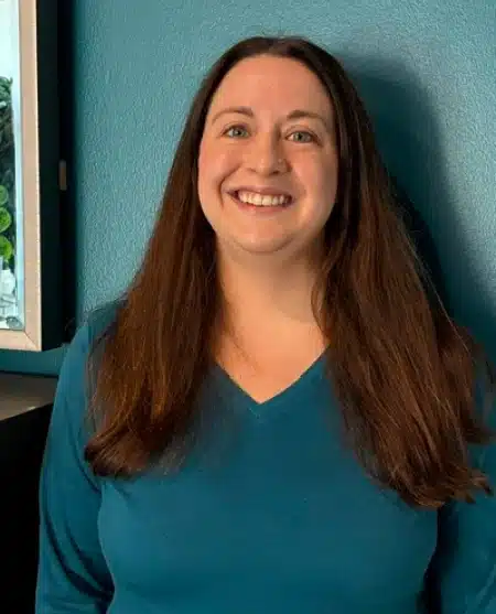 Woman with long dark hair smiling at camera against blue background, professional headshot.