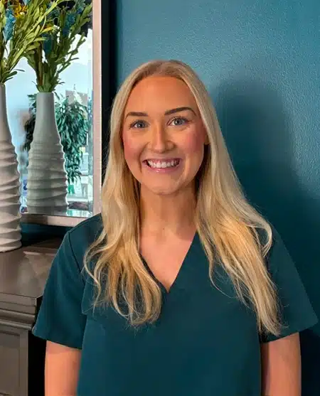 Woman smiling at camera wearing dental-themed shirt against blue background.